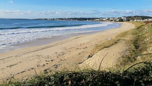A beach with a sandy shore, a fence, and houses in the background. - Spacious Coastal Duplex Cottage for 8 (Audierne)