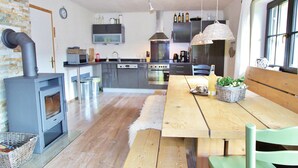 A modern kitchen with a wood-burning stove, a dining table with benches, and a view of the adjacent living area. - Chalet Near Skilift & Bikepark in Leogang (Leogang)