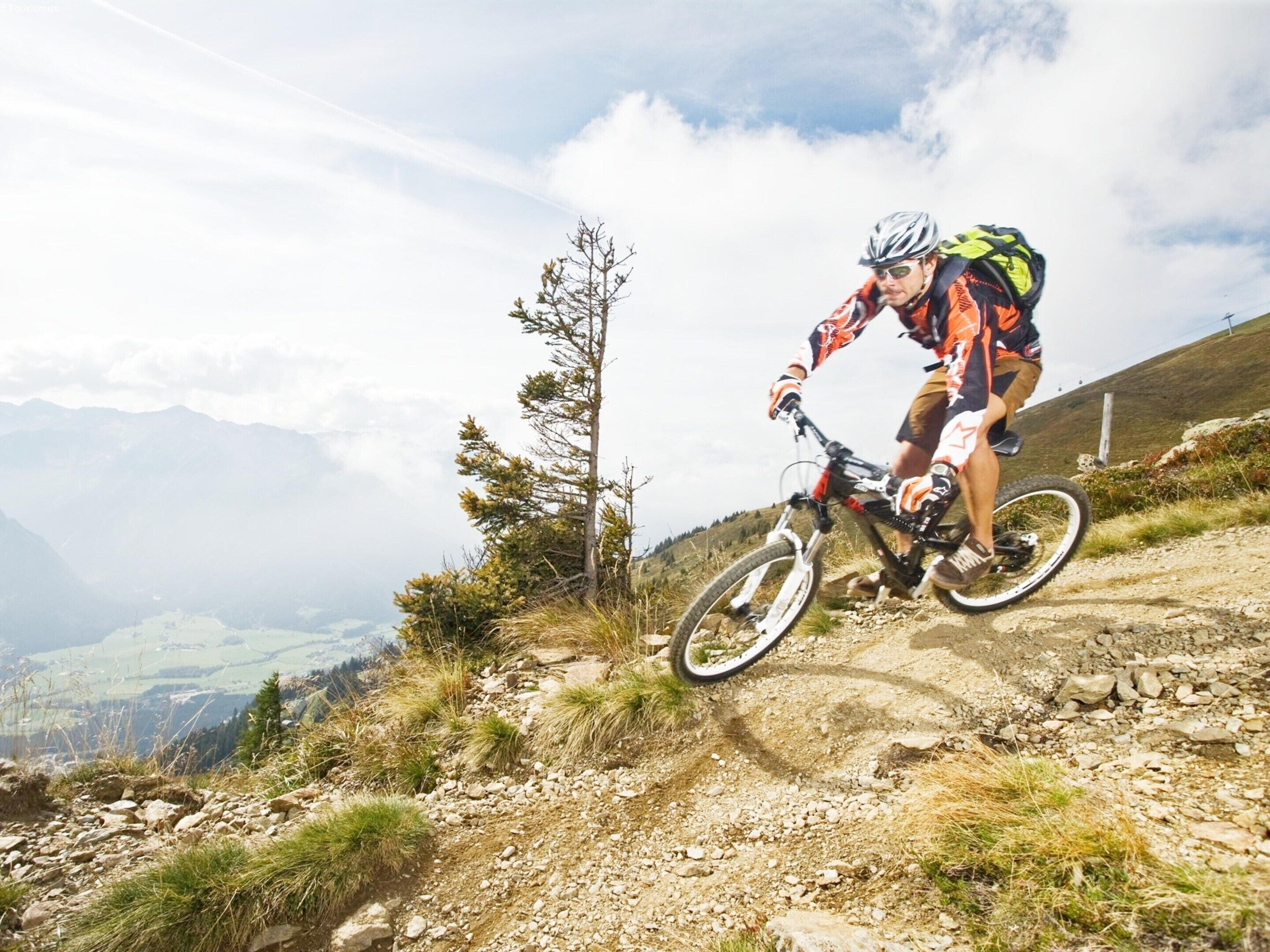 A mountain biker on a dirt trail with a view of mountains and a clear sky.