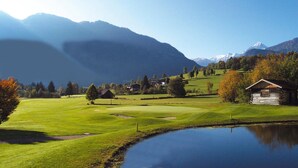 A golf course with a pond, houses, and mountains in the background. - Chalet Near Skilift & Bikepark in Leogang (Leogang)