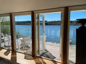 Una terraza con puerta de vidrio que da a vistas de un lago, mobiliario exterior y piso de madera.