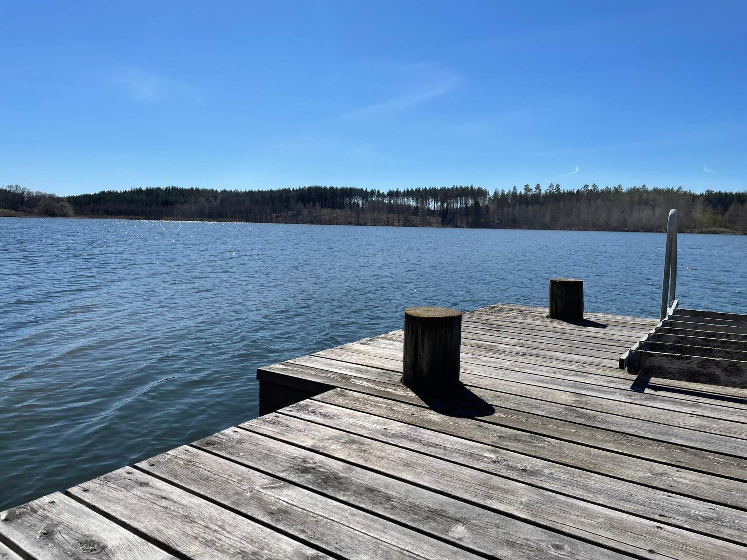 A wooden dock extending into a calm lake with a forested shoreline in the background.