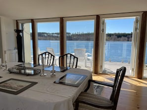 A dining area with a table set for four, large windows, and a view of a lake. - 5 Star Holiday Home in Mariefred (Mariefred)