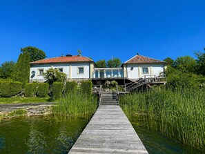 A house with a wooden dock leading to a bridge over water, surrounded by greenery. - 5 Star Holiday Home in Mariefred (Mariefred)