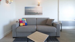 Ein modernes Wohnzimmer mit einem grauen Sofa, einem Holztisch und einem Bild von einer Strandlandschaft.