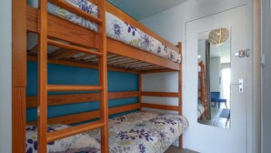 Ein Stockbett mit floralem Bettzeug, eine Tür mit Spiegel und ein blauer Stuhl im Hintergrund.