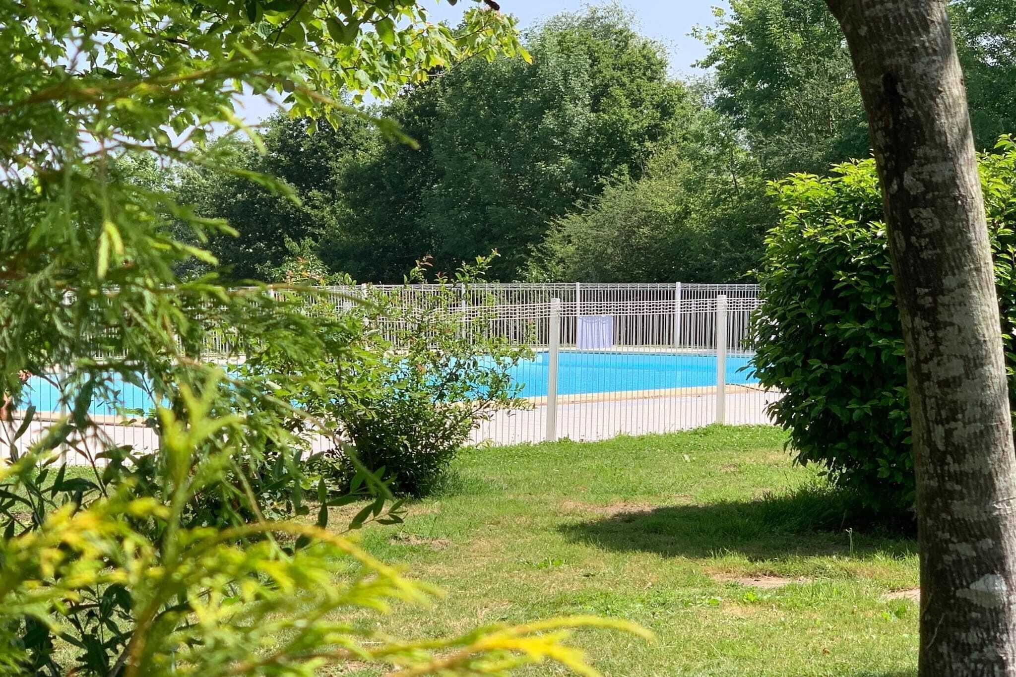 Una piscina rodeada por una cerca blanca, con árboles y césped al fondo.
