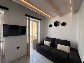 A modern living room with a flat-screen TV, a black sofa with cushions, and decorative wall art. - Symi Duo B - Double Studio (Simi)
