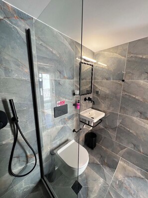 A modern bathroom with a glass-enclosed shower, a white sink, and a toilet. - Symi Duo B - Double Studio (Simi)