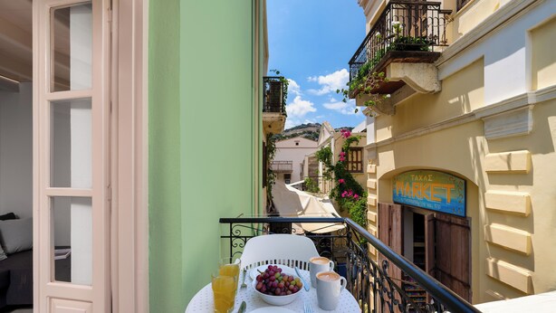 Ein Balkon mit Frühstückstisch, Blick auf einen Markt und ein Gebäude mit einem Schild.