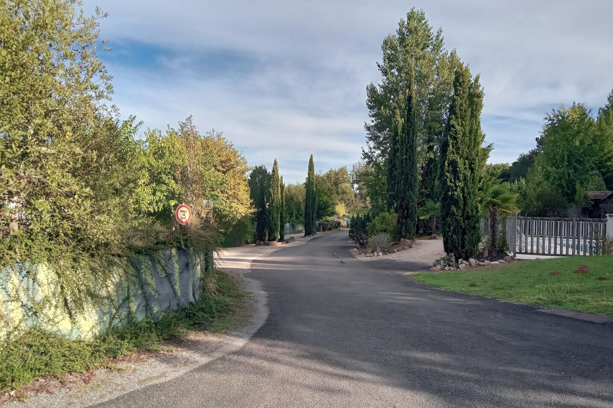 A road curving through a residential area with trees and a gated entrance.