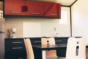 A modern kitchen with wooden cabinets, a black countertop, and a dining area with a table and chairs. - Accessible Family Cottage in Marminiac (Marminiac)