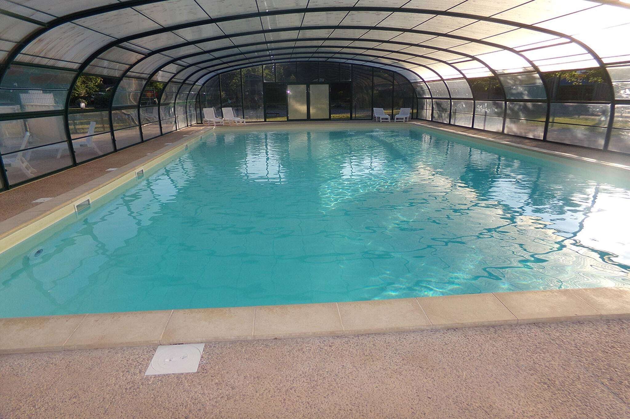 Une piscine intérieure dotée d’un toit incurvé, d’une eau cristalline et de chaises longues disposées le long des bords.