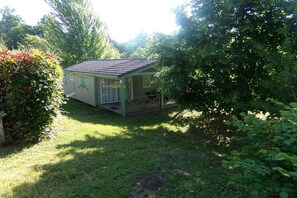 Une petite maison à un seul étage, dotée d’un porche et entourée d’une végétation luxuriante.