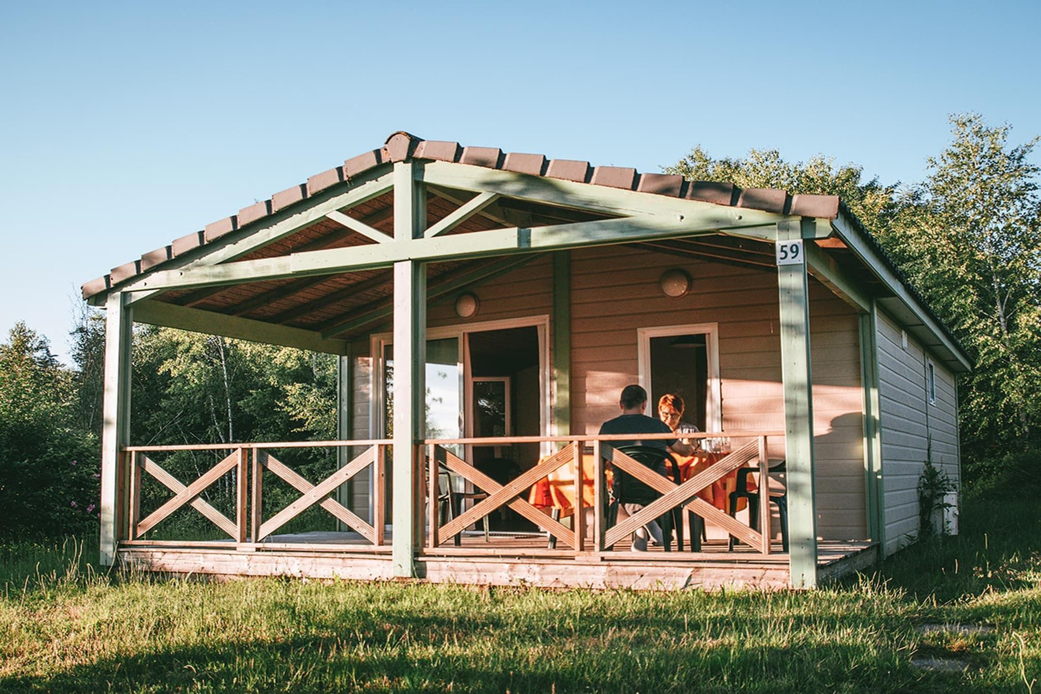 A small wooden cabin with a porch, numbered 59, surrounded by greenery.