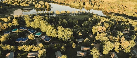An aerial view of a campground with multiple cabins, a lake, and surrounding forested hills.
