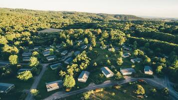 Vue aérienne d’un quartier résidentiel composé de nombreuses maisons individuelles, entouré d’une forêt dense et de collines.
