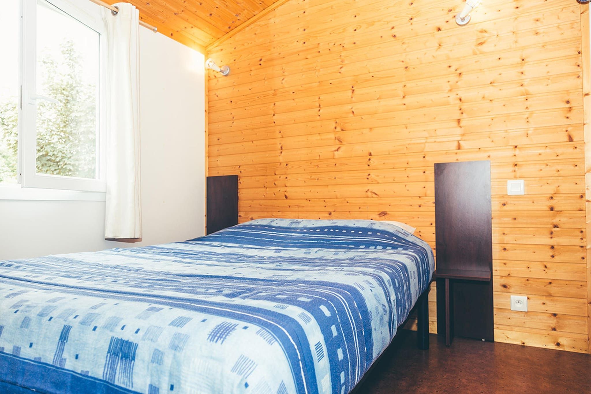 Una stanza con rivestimenti in legno, un letto, una finestra e due altoparlanti.