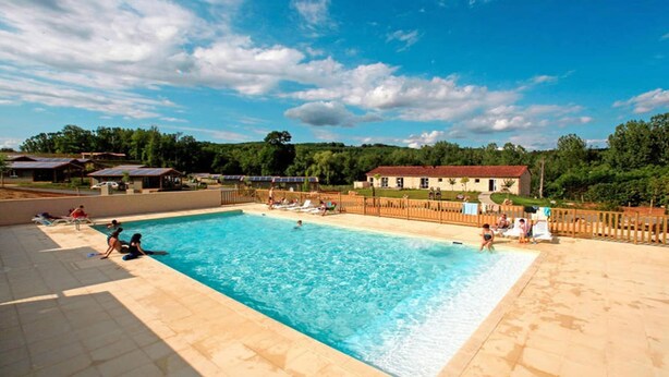 A swimming pool with people around it, a fenced area, and buildings in the background. - Spacious Cottage for 6 in Marminiac (Marminiac)