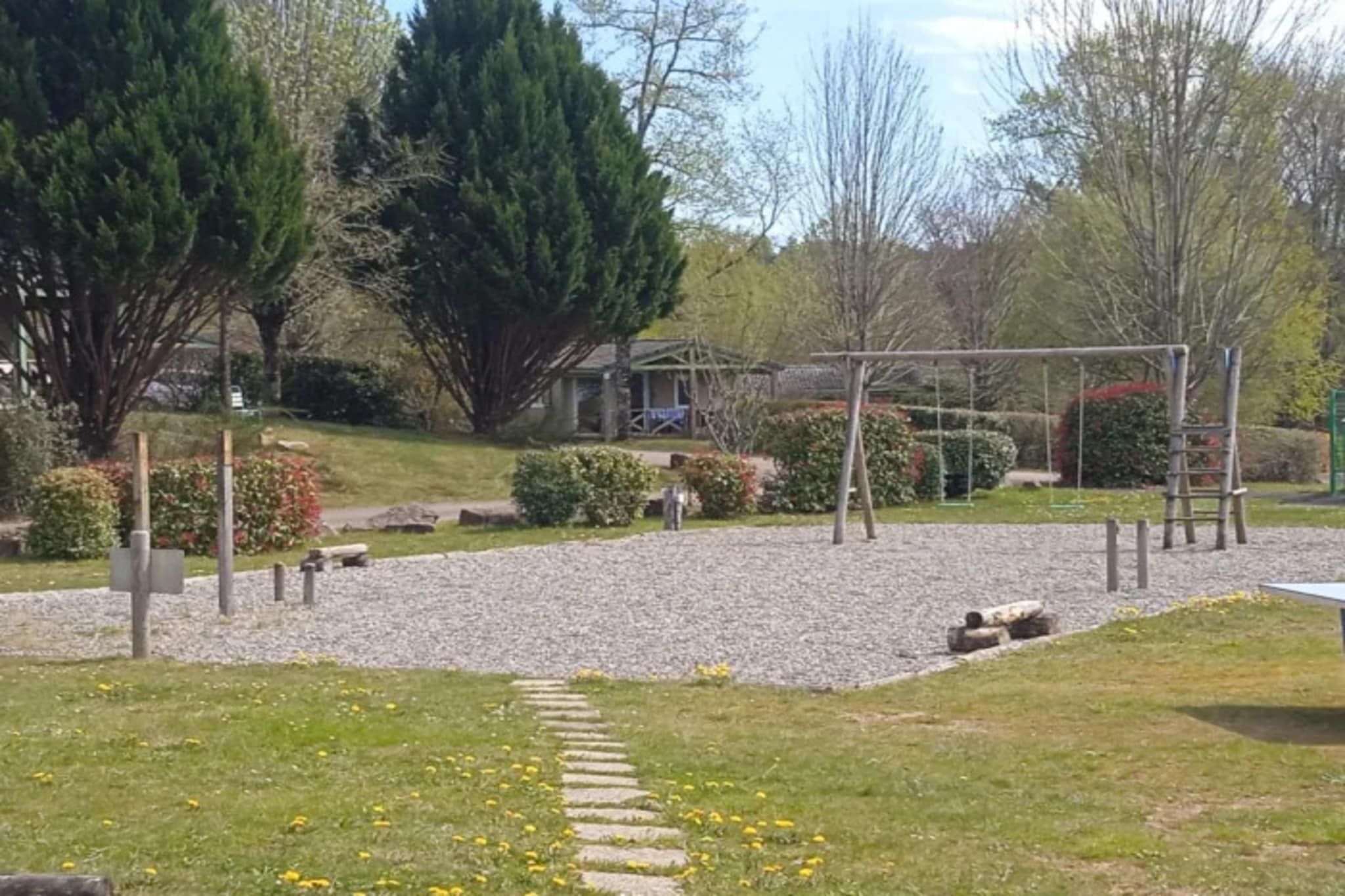 Un parc infantil amb un camí de grava, arbres i una zona enjardinada.