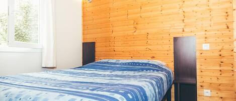 Una habitación con paneles de madera, una cama, un ventanal y dos altavoces.