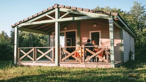 Een klein houten vakantiehuisje met een veranda, nummer 59, omringd door groen.