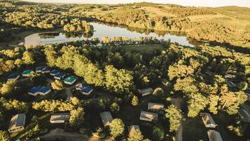 An aerial view of a lakeside property with multiple cabins and a central building, surrounded by dense forest and hills.