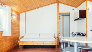 Een houten interieur met een bed, een eettafel met stoelen en een witte muur.