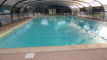Uma piscina interior com teto curvo, água cristalina e espreguiçadeiras ao longo das bordas.