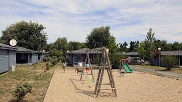Un'area giochi con altalene e scivolo, circondata da case e alberi.