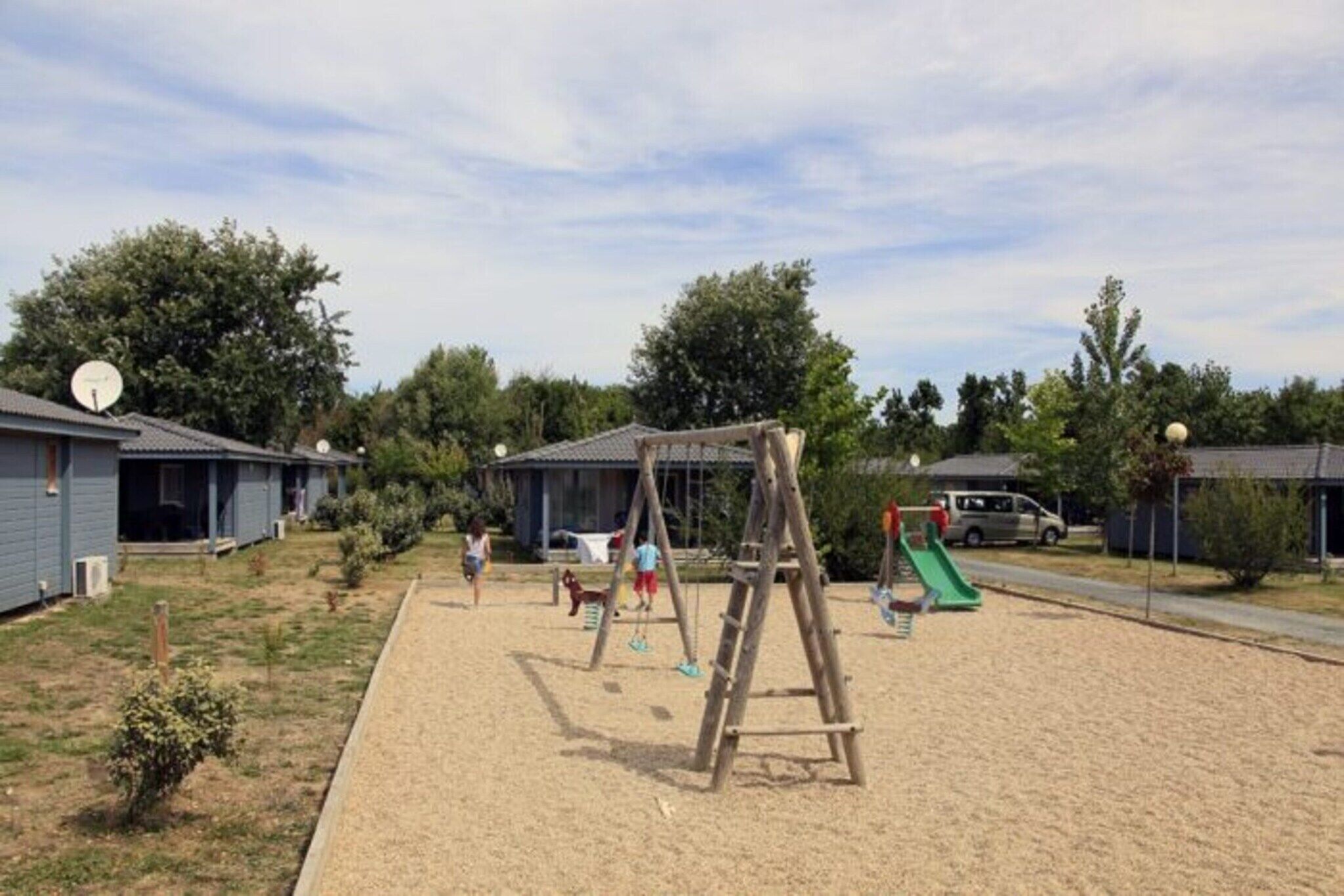 Un parque infantil con columpios y un tobogán, rodeado de casas y árboles.