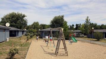 Un parque infantil con columpios y un tobogán, rodeado de casas y árboles.