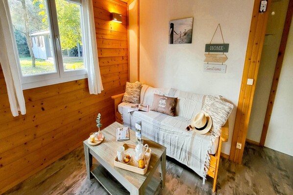 Ein gemütliches Zimmer mit Holzboden, einer Couch mit Kissen, einem Couchtisch mit Tablett und einem Fenster mit Vorhängen.