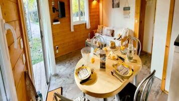 Interior de una cabaña de madera con una mesa de comedor dispuesta para cuatro personas, un sofá y un televisor montado en la pared.