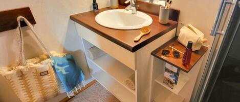 A bathroom with a sink, mirror, towel rack, and a small shelf with toiletries.