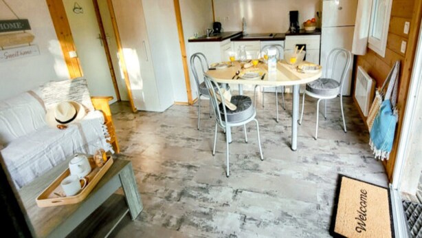 A cozy living room with a sofa, a coffee table with cups and saucers, and a dining area with a table and chairs. - Coastal Family Cottage for Six (Saint-Denis-d'Oléron)