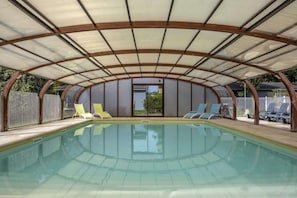 Piscina coberta com teto curvo, rodeada por espreguiçadeiras.