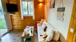 Interior acogedor de una cabaña con revestimiento de madera, un sofá, una mesa con objetos y un televisor montado en la pared.