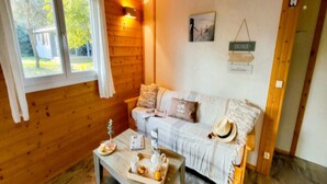 Una habitación acogedora con piso de madera, un sofá blanco con cojines, una mesa de centro con una bandeja y una ventana con cortinas.