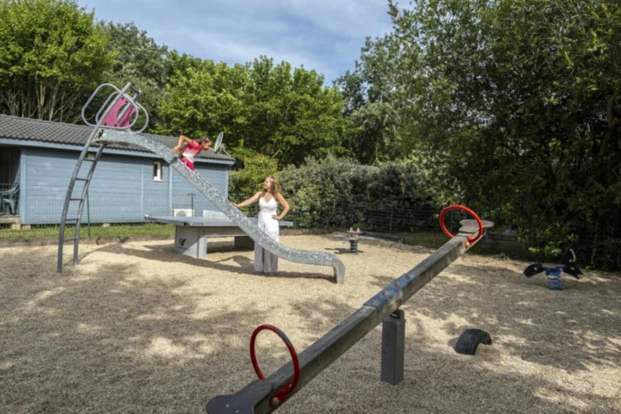A playground with a slide, a seesaw, and a basketball hoop.