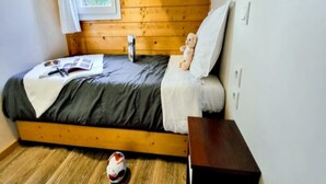Una cama individual con cabecera de madera, una mesita de noche, una ventana con vistas a zonas verdes y un par de zapatos en el suelo.