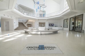Un vaste atrium doté d’un espace de repos central, d’un escalier et d’une grande porte vitrée sur le côté droit.