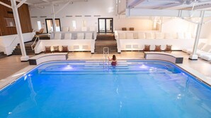 A large indoor swimming pool with a central staircase, white lounge chairs, and a modern interior design. - Spa Retreat in La Roche-Posay (La Roche-Posay)