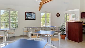Un espace repas avec des tables et des chaises, de grandes fenêtres et une vue sur les arbres.