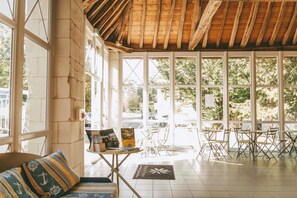 A spacious room with a high ceiling, large windows, and a wooden ceiling. There is a seating area with a sofa and a table with chairs. - Family Stay in La Roche-Posay for 6 (La Roche-Posay)
