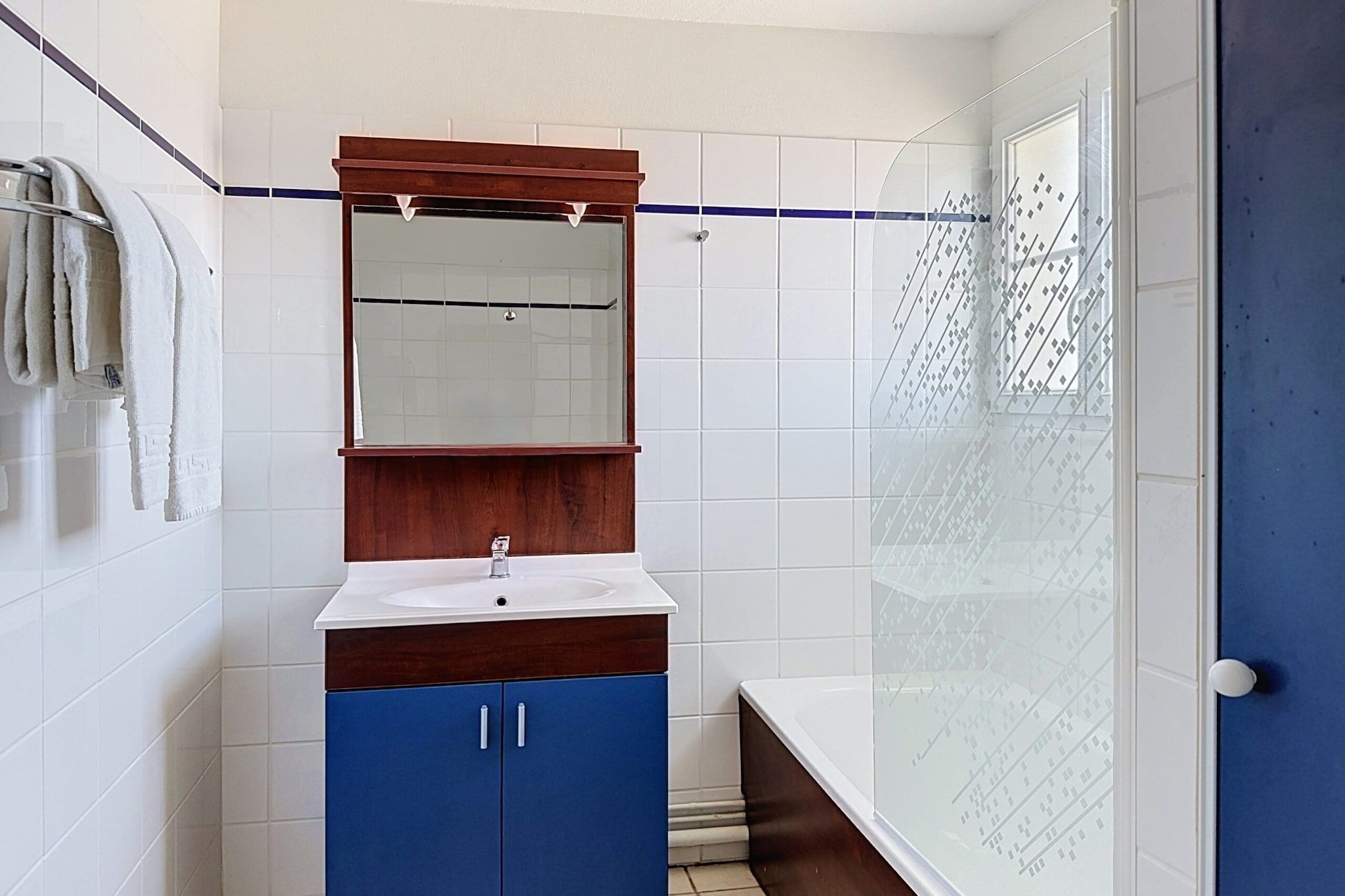 Een badkamer met een witte wastafel, een spiegel erboven en een blauwe kast eronder.