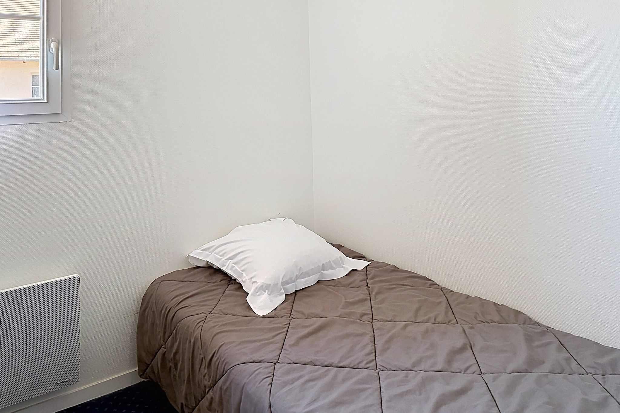 A small, single-bed room with a brown bedspread and a white pillow.