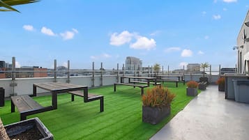 A rooftop terrace with artificial grass, outdoor seating, and a view of the city skyline.