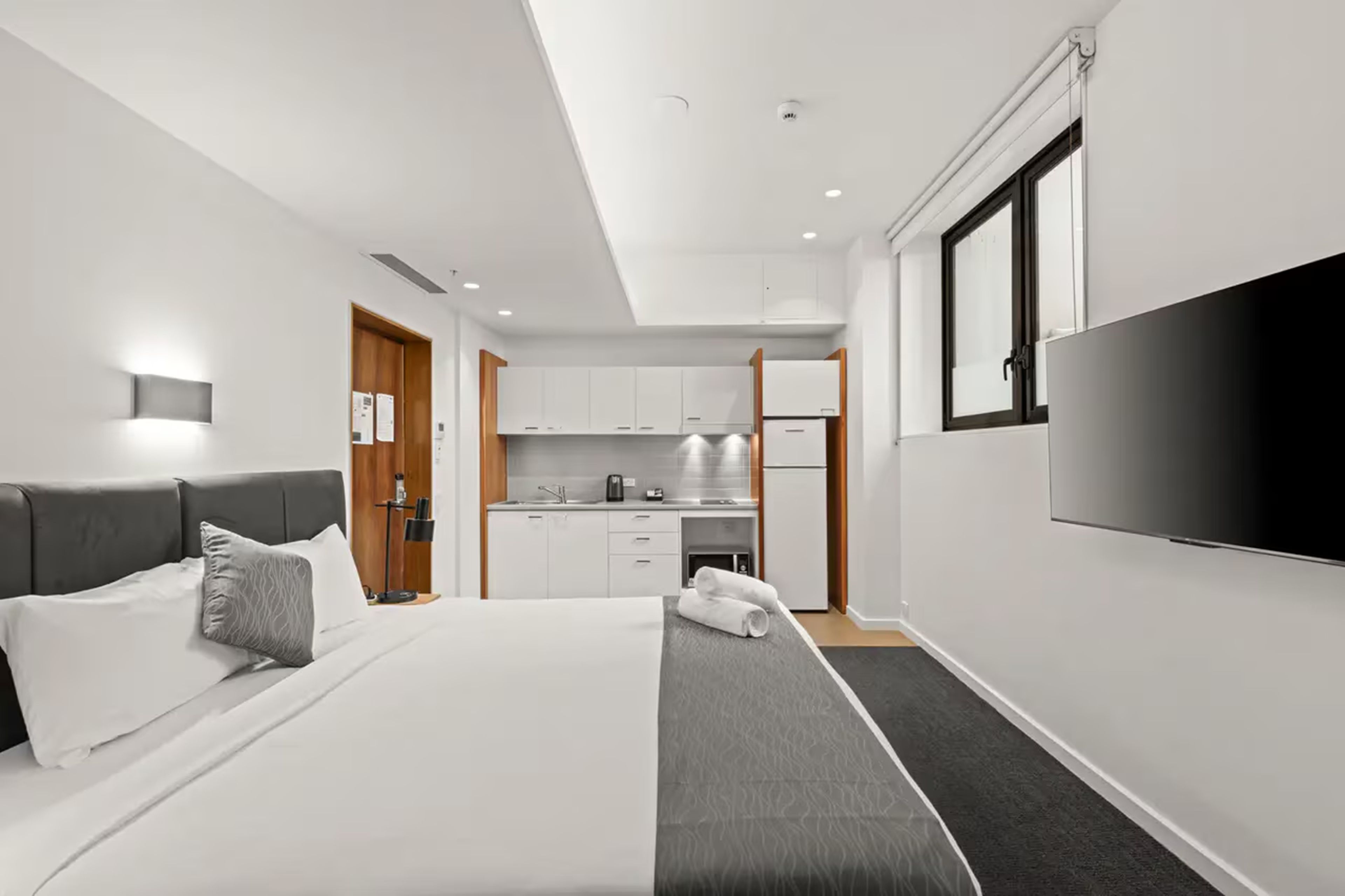 Een moderne hotelkamer met een bed, een televisie, een kitchenette en een badkamer.