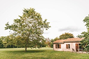 A small building with a tiled roof, a grassy area, and a large tree in the foreground.